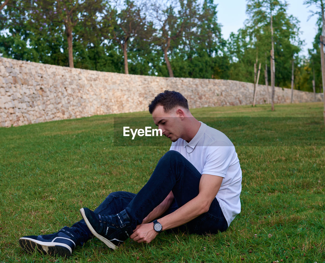 A young man posing relaxed on the grass in a park.