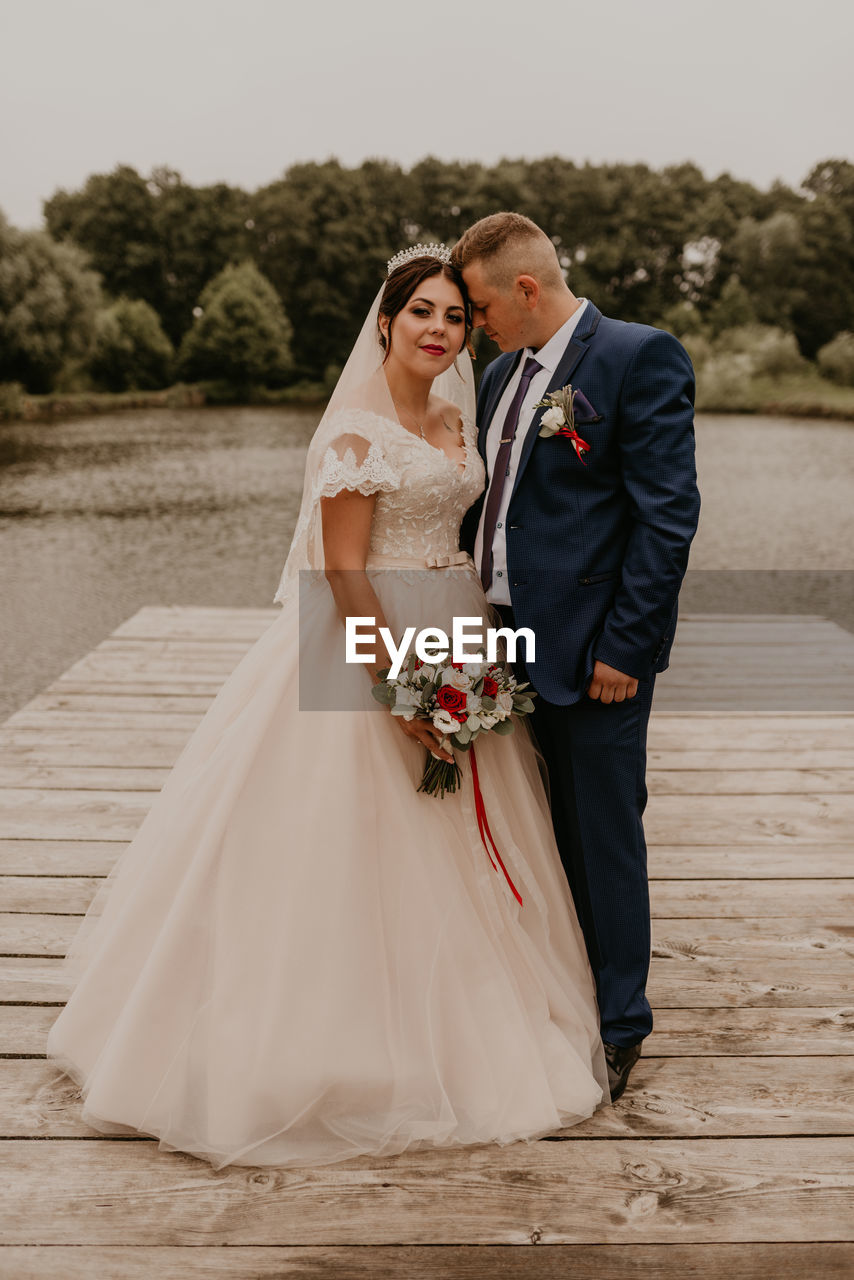 rear view of bride and groom standing on pier at park