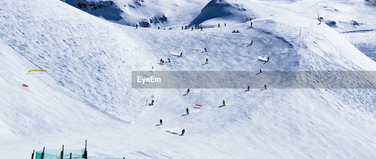 AERIAL VIEW OF PEOPLE SKIING ON SNOWCAPPED MOUNTAIN