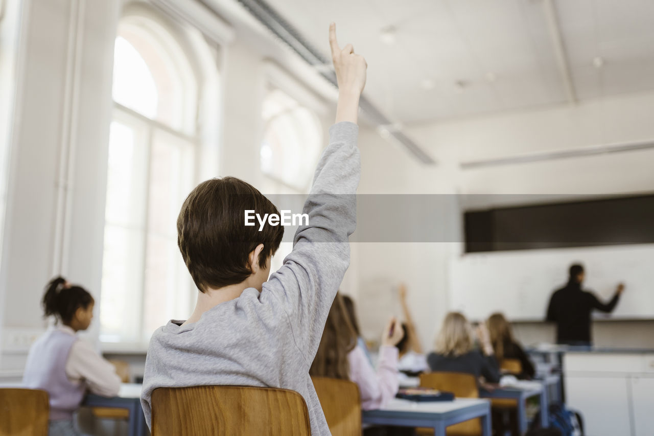 Boy raising hand while attending lecture in classroom