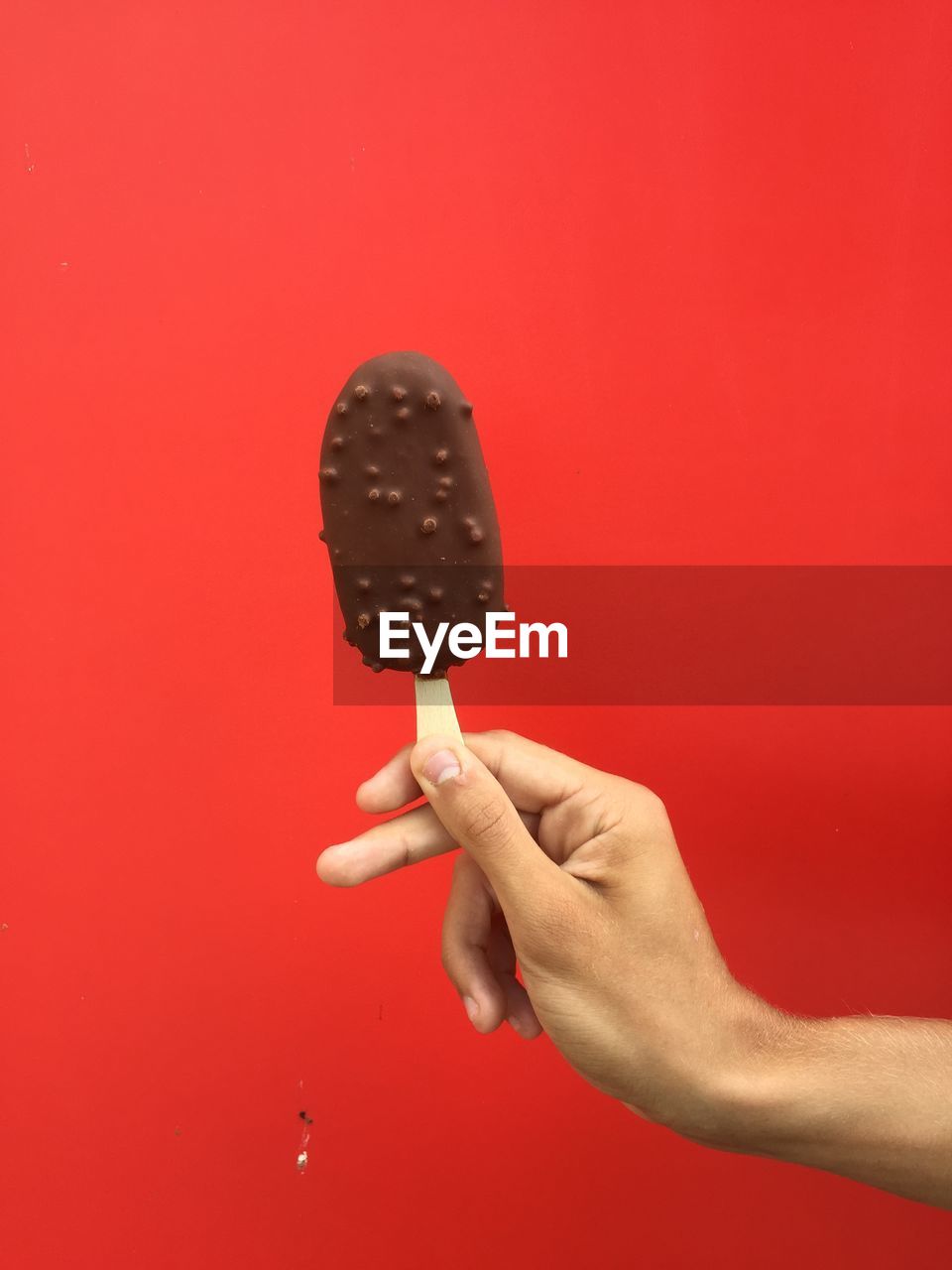 Cropped image of person holding ice cream against red background