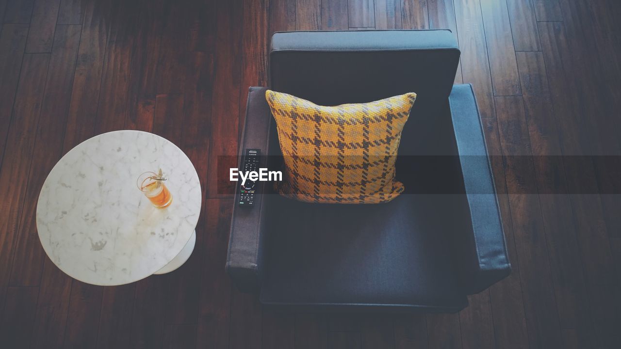 High angle view of cushion and remote control on armchair by coffee table