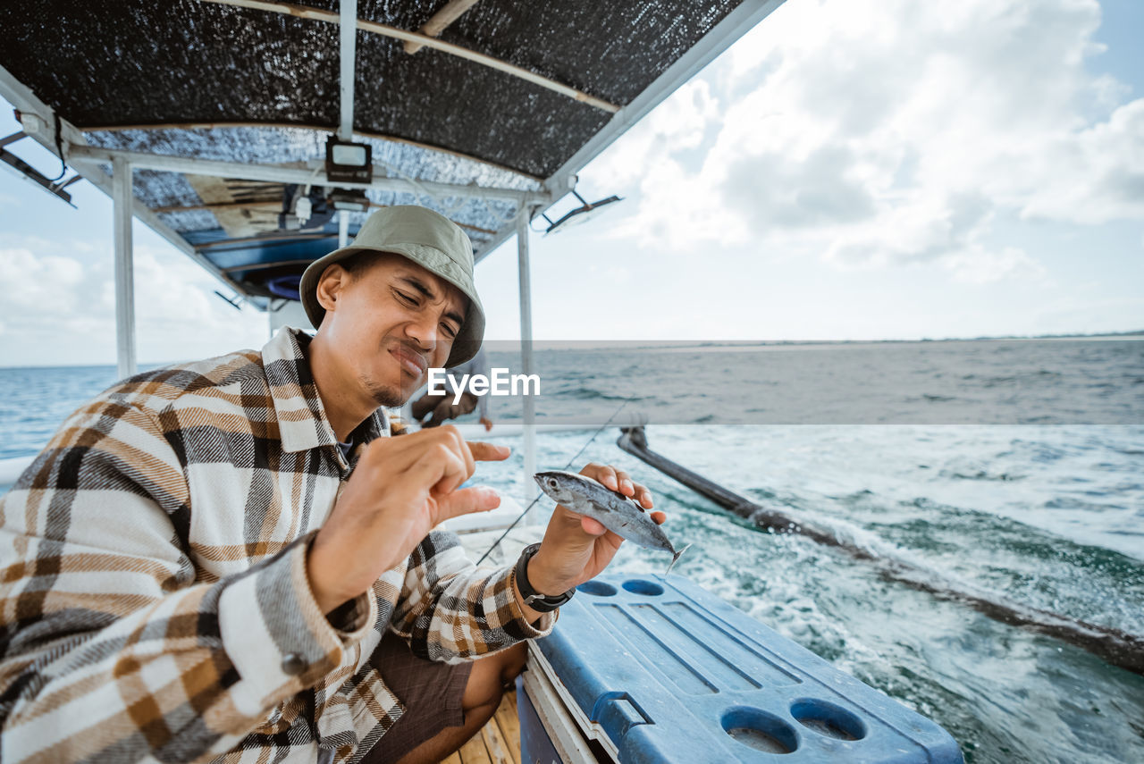 portrait of young man drinking water while sitting on boat