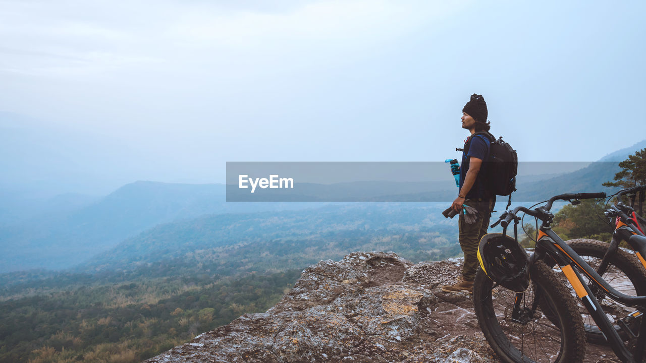 Man with bicycles standing on mountain during foggy weather