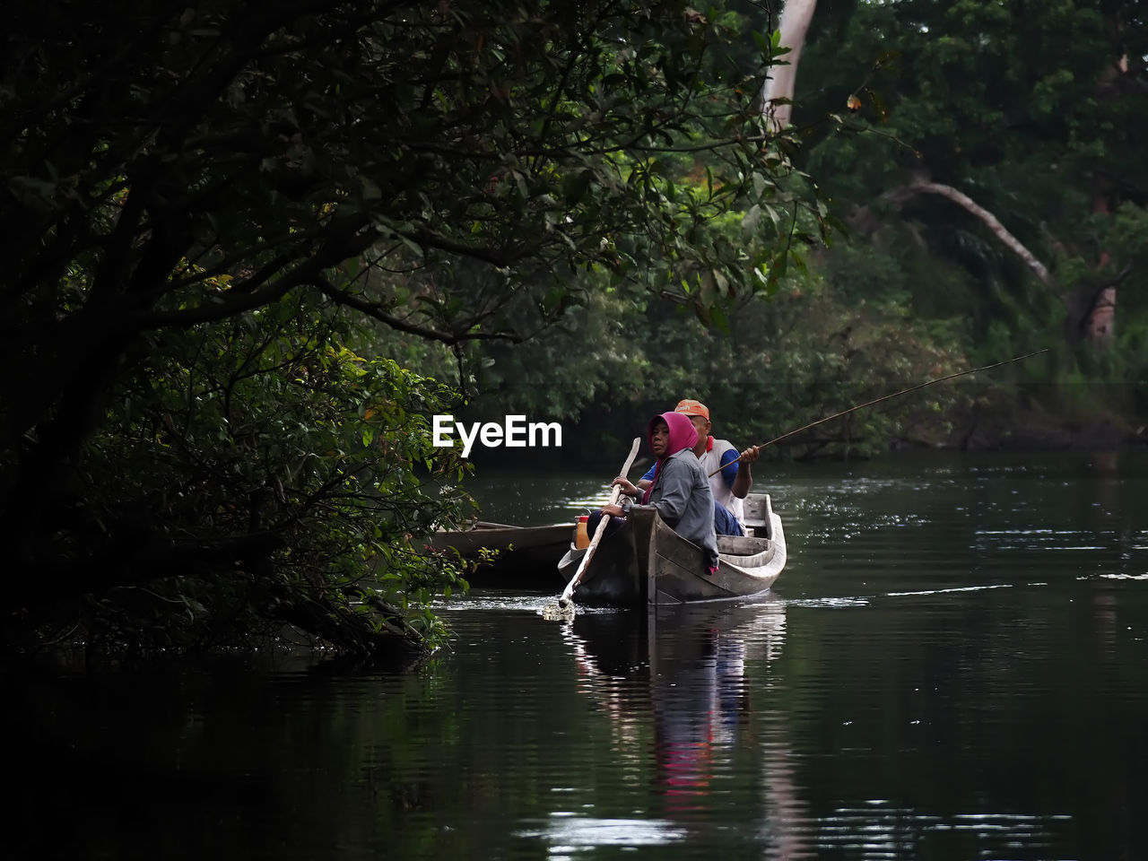 People in boat on river amidst trees in forest