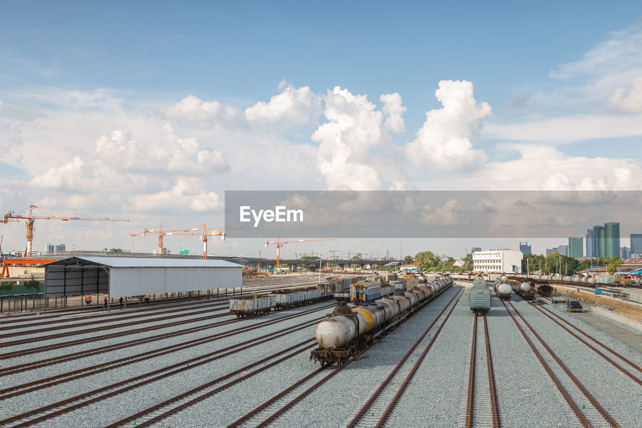 Trains on railroad tracks in city against cloudy sky