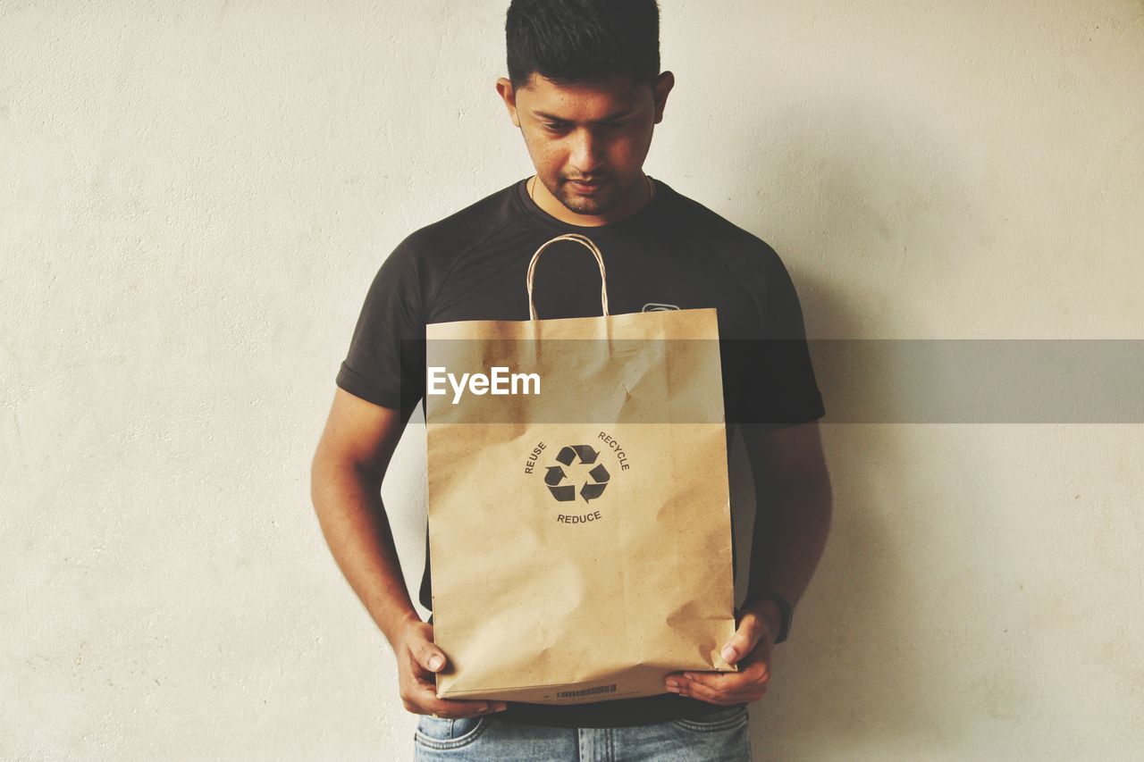 Man with shopping bag standing against wall