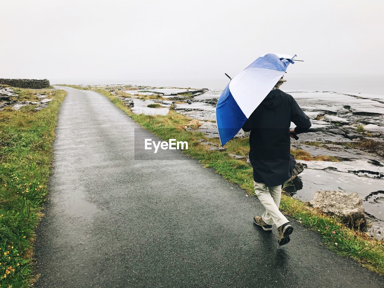 Rear view of man walking on road during rainy season