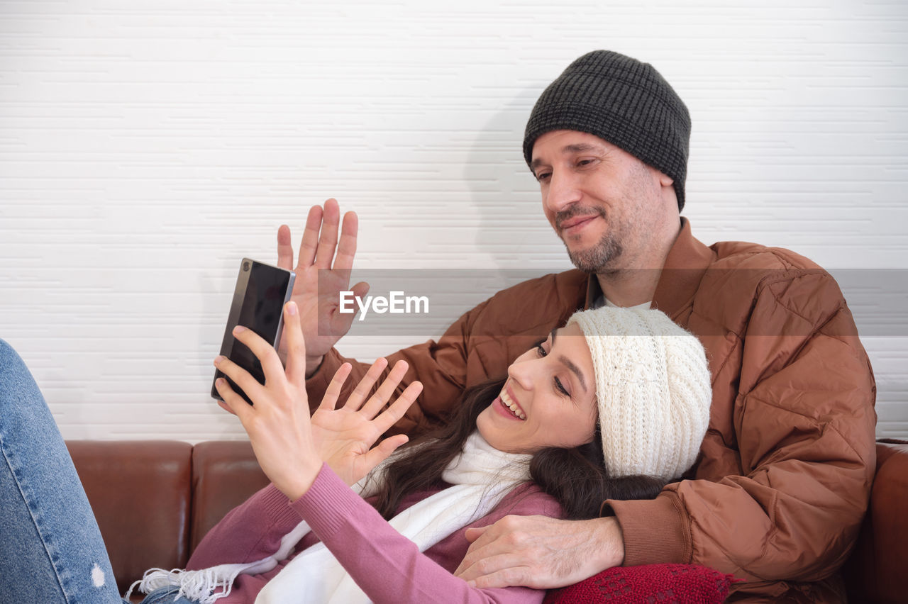 Happy couple greeting in a phone video call while relaxing on sofa in living room at home