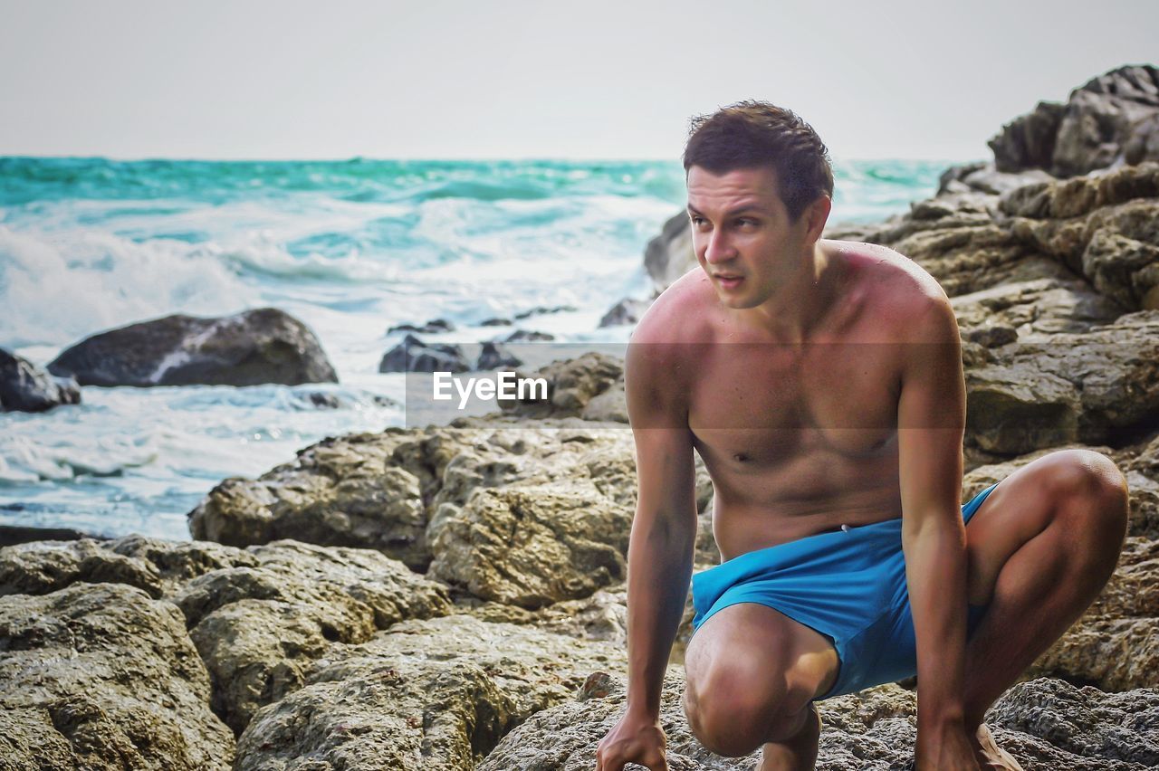 YOUNG MAN SITTING ON ROCK BY SEA