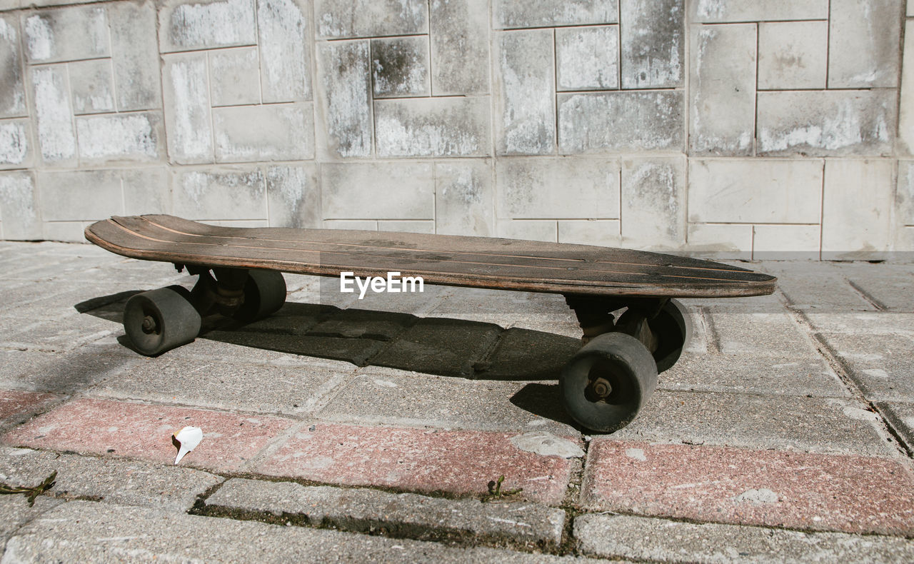 Wooden skateboard on footpath against wall
