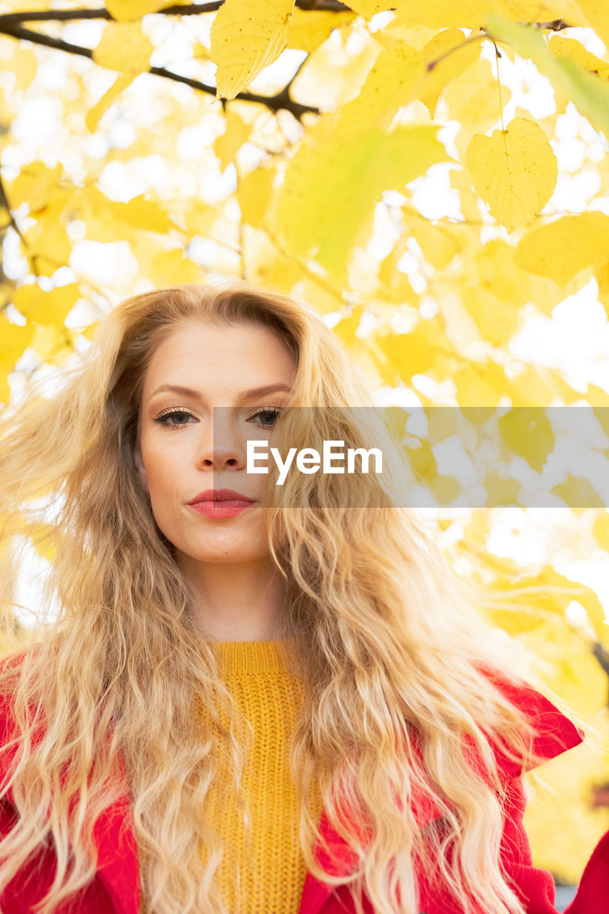 PORTRAIT OF YOUNG WOMAN WITH LEAVES IN BACKGROUND