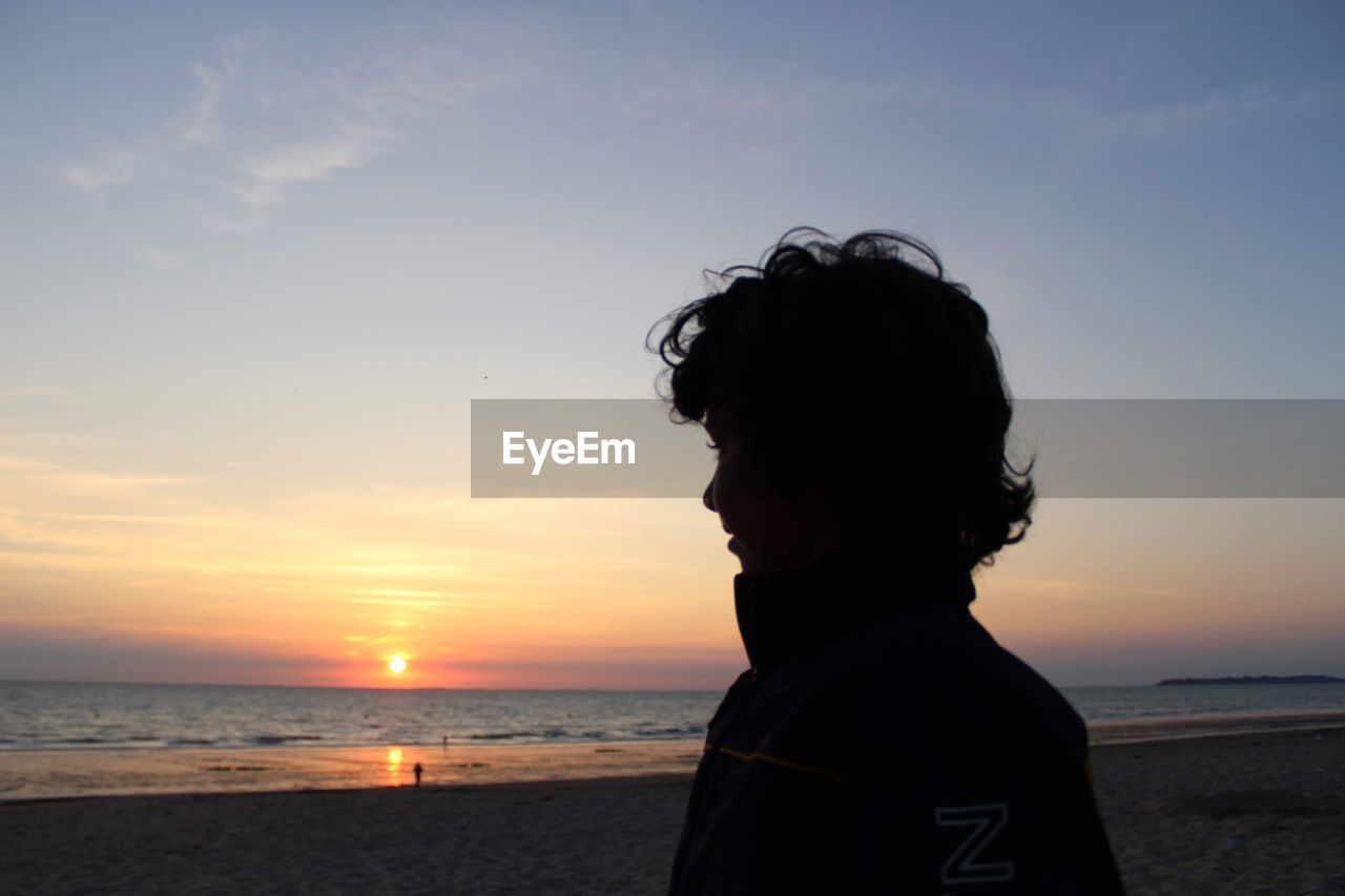 Silhouette man standing at beach against sky during sunset