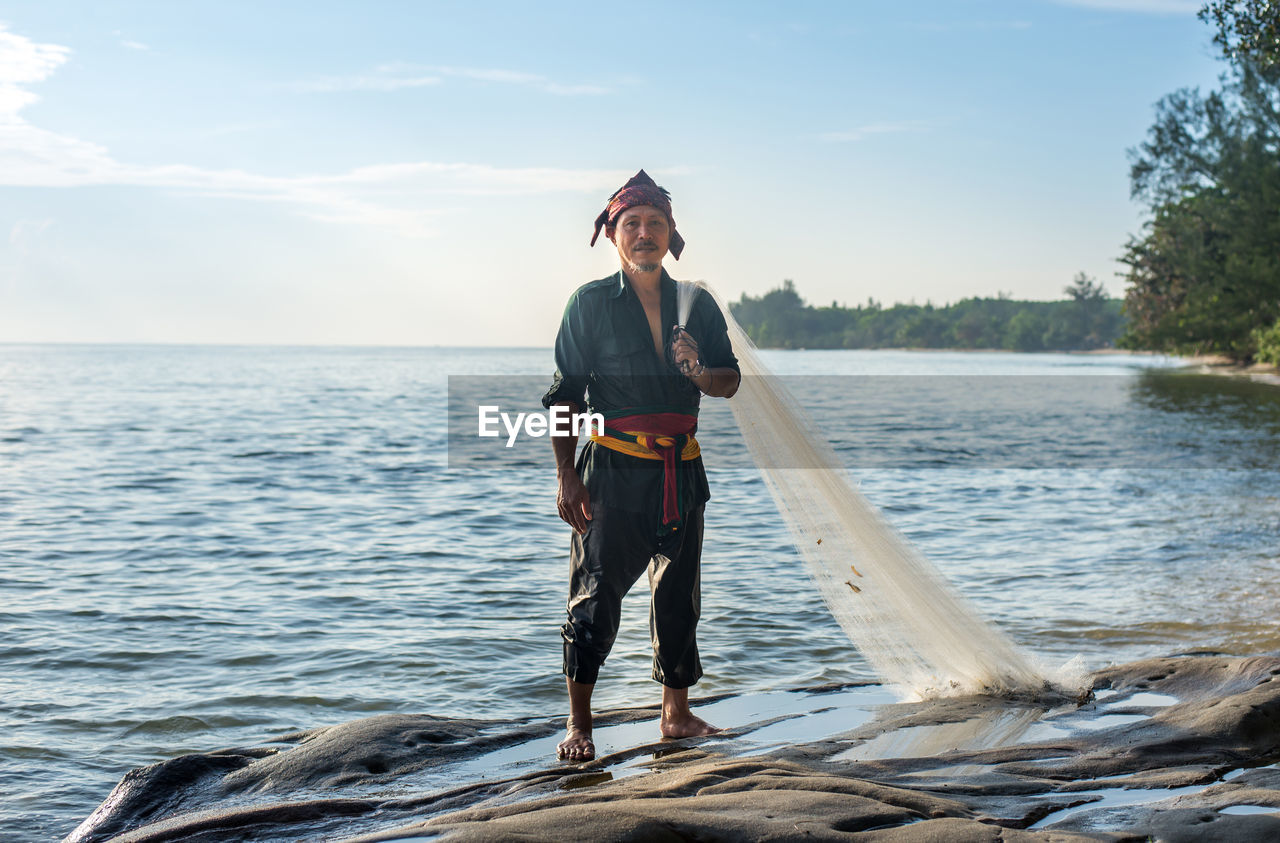 Portrait of fisherman standing by sea against sky