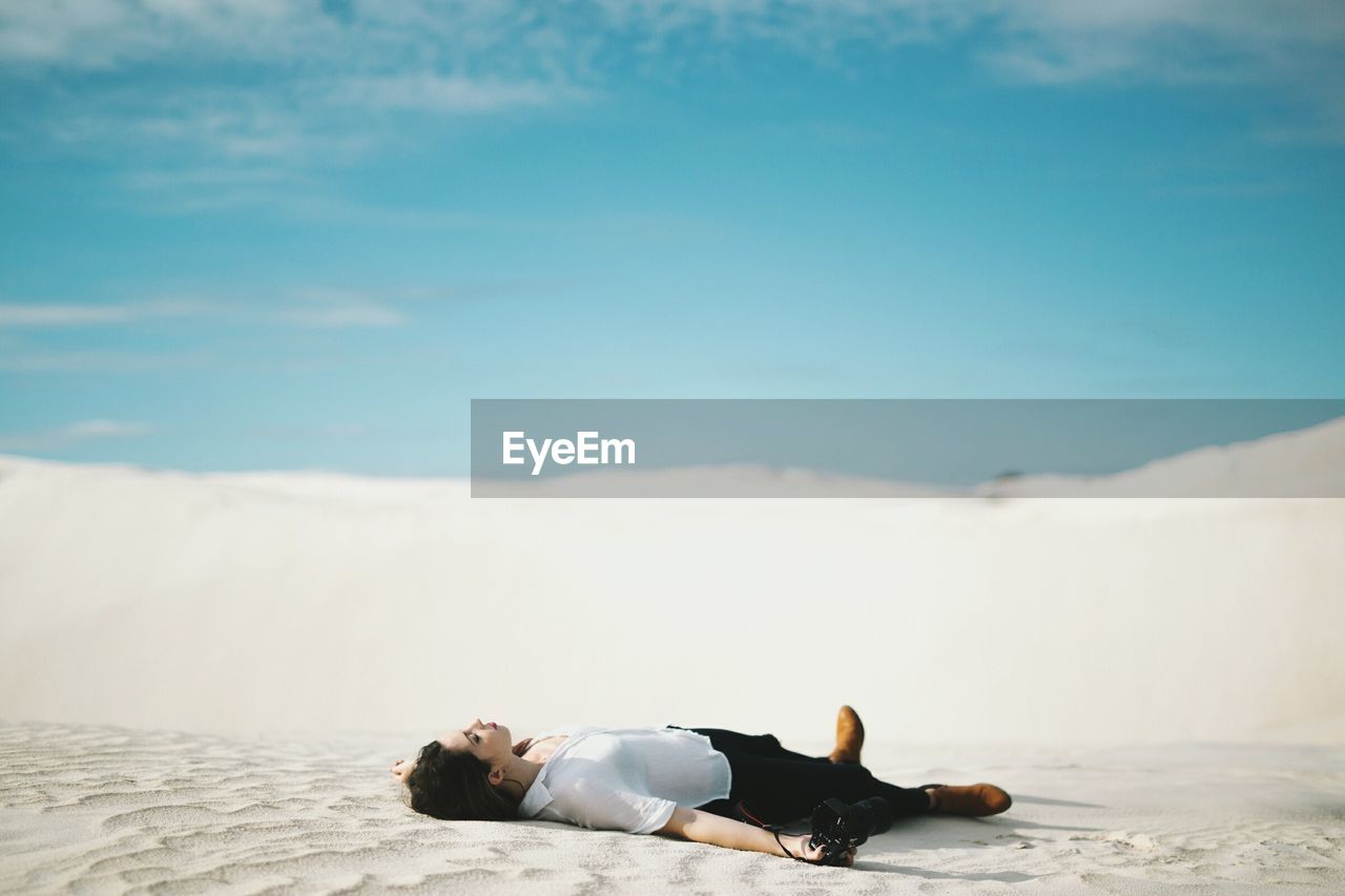 Full length of woman holding camera lying on sand at desert against sky