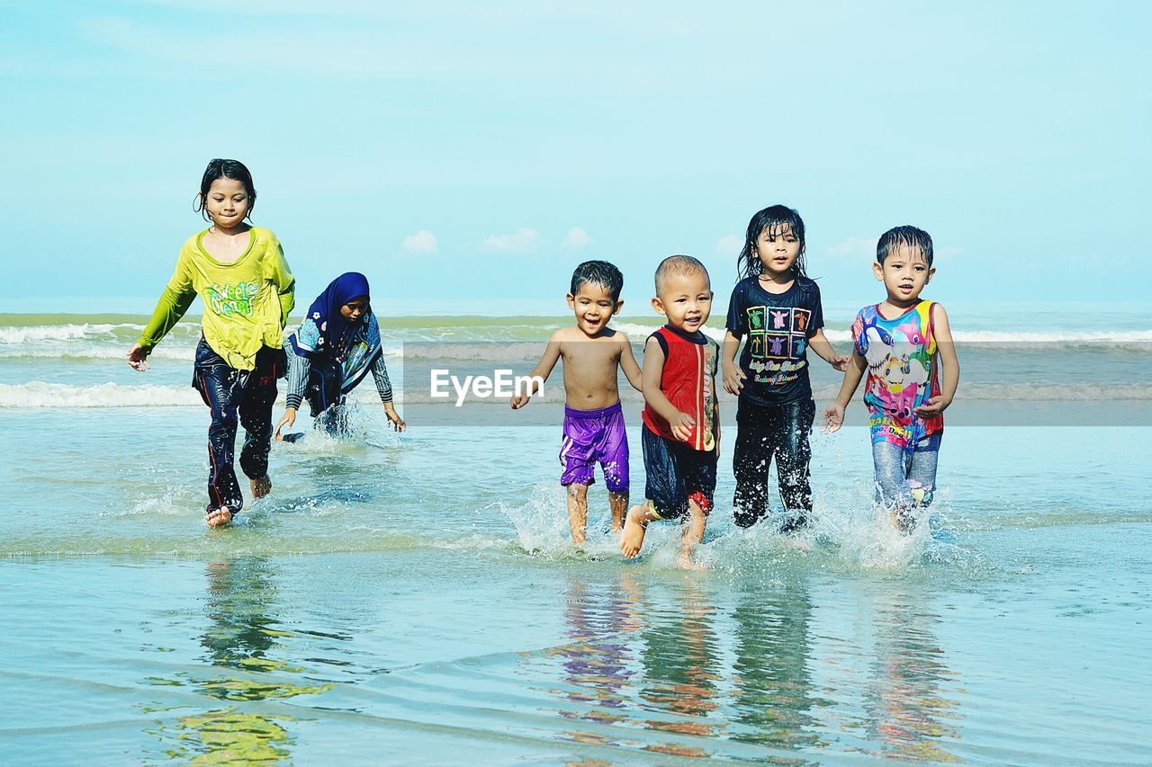 Playful children running in sea against sky