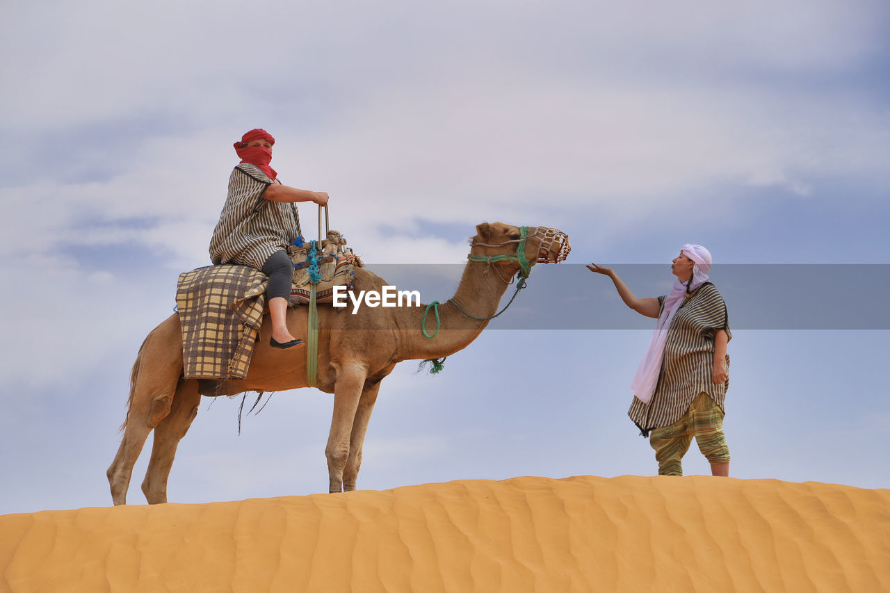 Woman looking at friends sitting on camel in desert