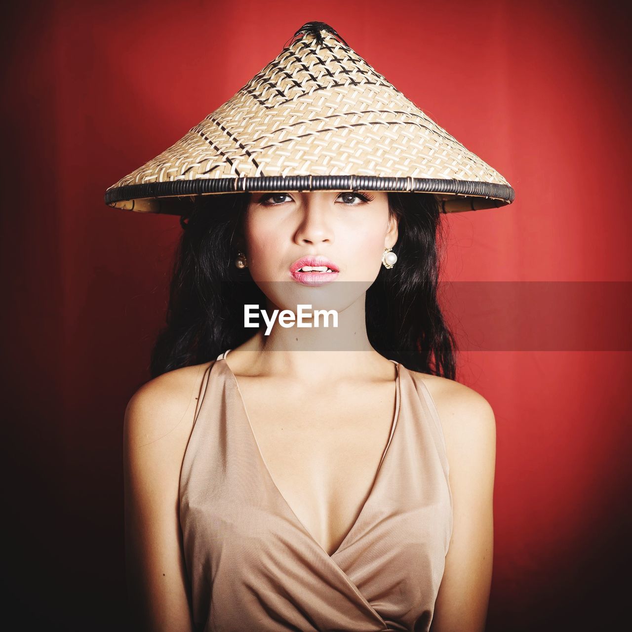 Portrait of beautiful young woman wearing asian style conical hat against red background
