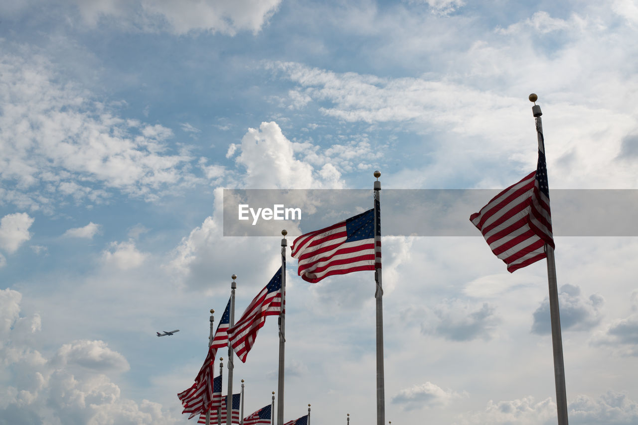 Low angle view of american flags waving against cloudy sky