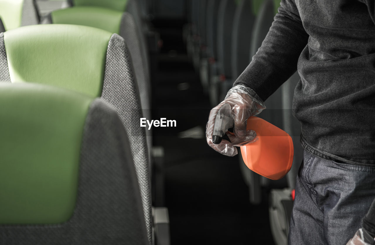 Coach bus driver cleaning and disinfecting vehicle seat armrests wearing vinyl gloves. 