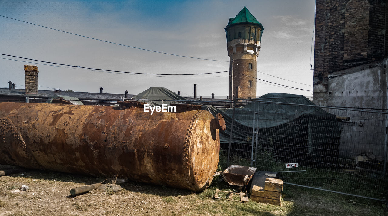 OLD RUSTY TOWER AMIDST BUILDINGS AGAINST SKY