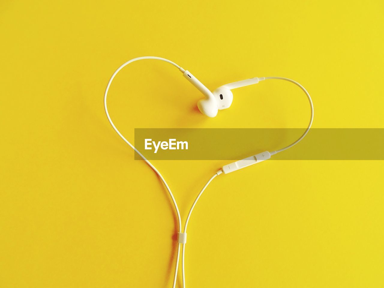 Heart shape formed of headphones over yellow background