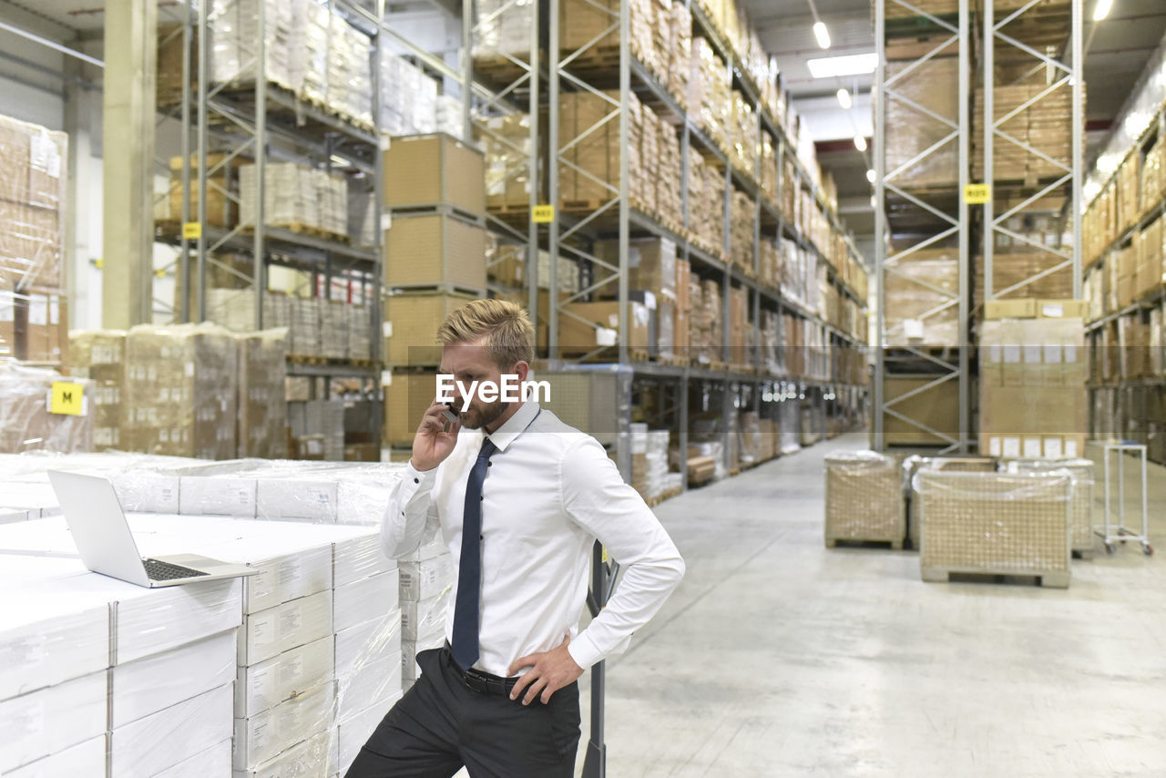 Businessman with laptop and cell phone in warehouse