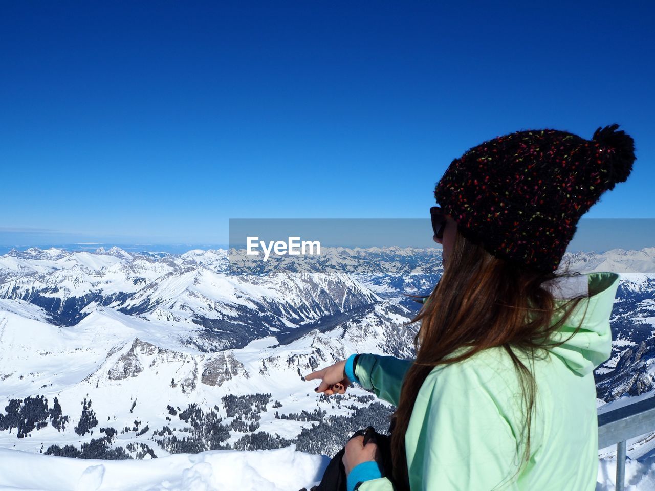 Woman looking at snow covered mountains against clear blue sky