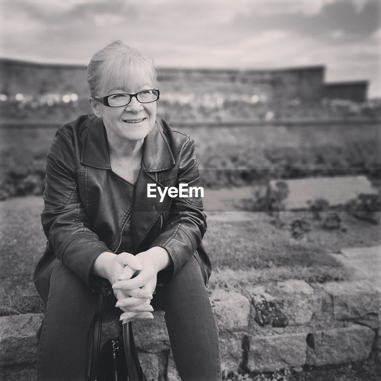 Smiling woman sitting on retaining wall outdoors