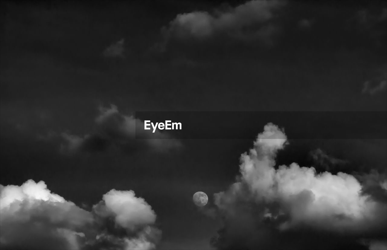 Low angle view of moon in cloudy sky at dusk