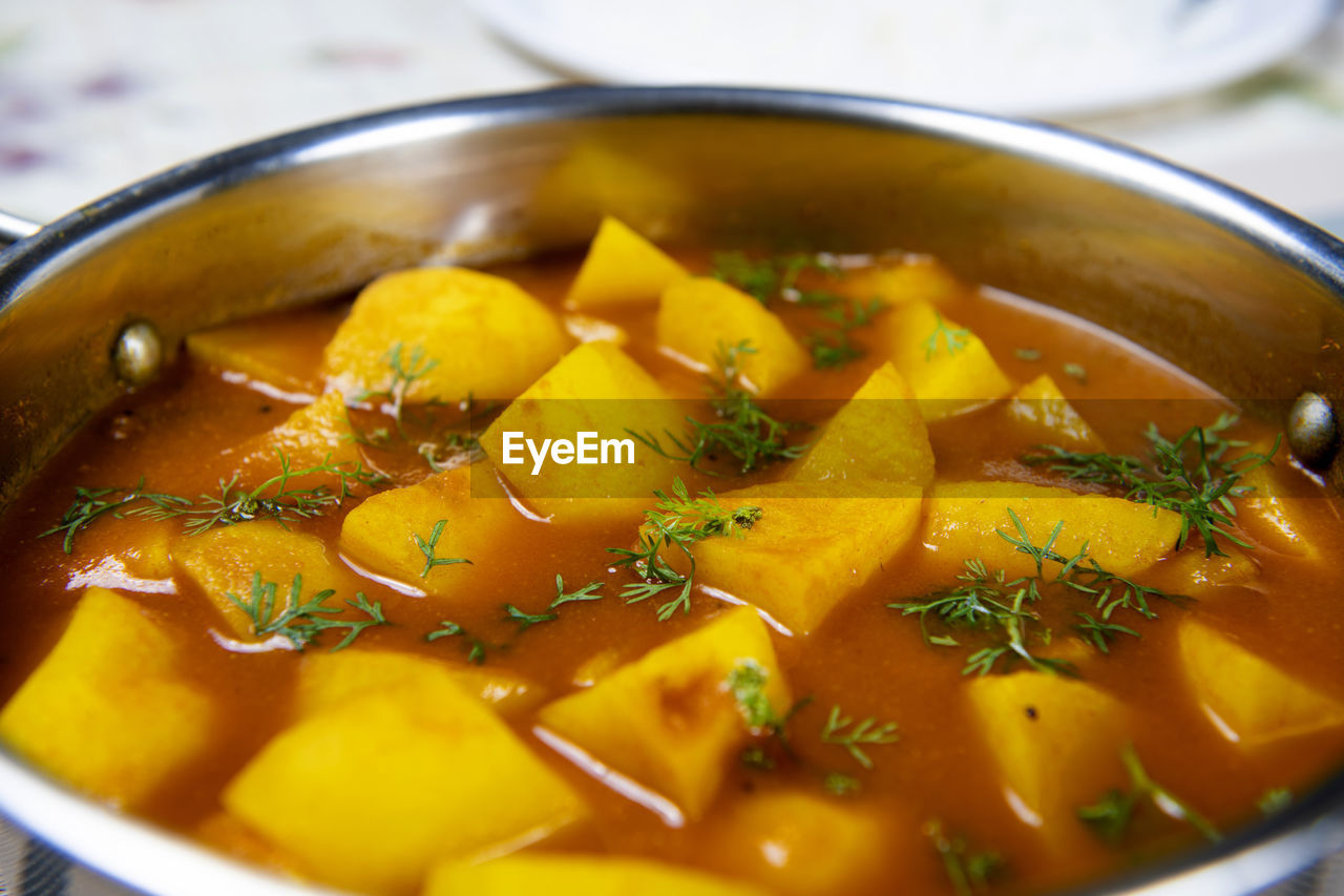 Potato chunks in tomato gravy served in a stainless bowl and garnished with coriander leaves.