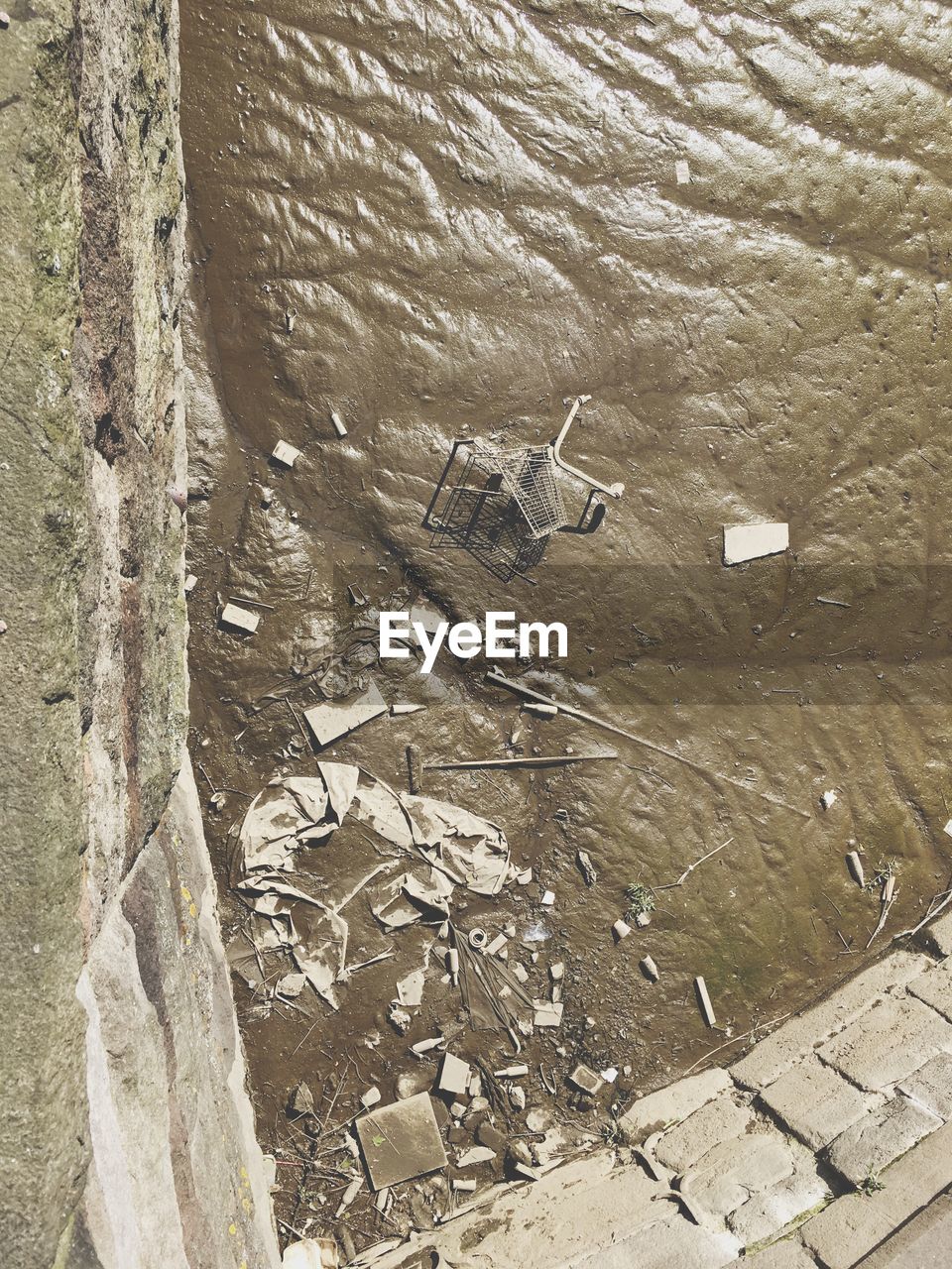 High angle view of abandoned and broken shopping cart on dirty riverbank