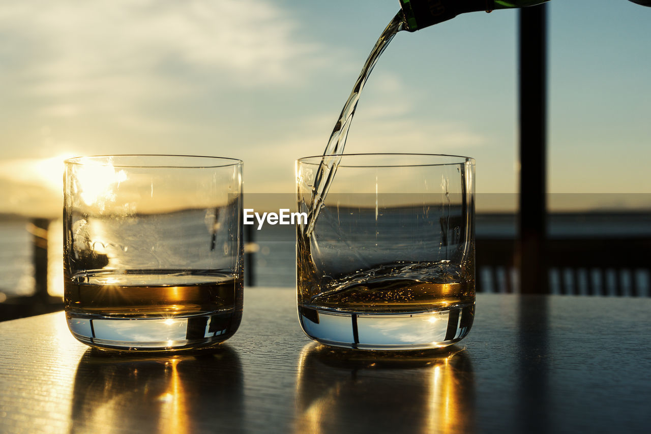 Close-up of whiskey pouring into glass on table against sky