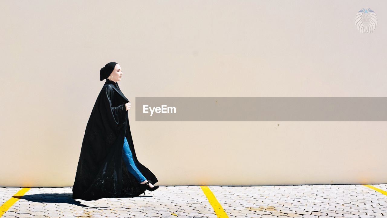 SIDE VIEW OF WOMAN STANDING ON WALL