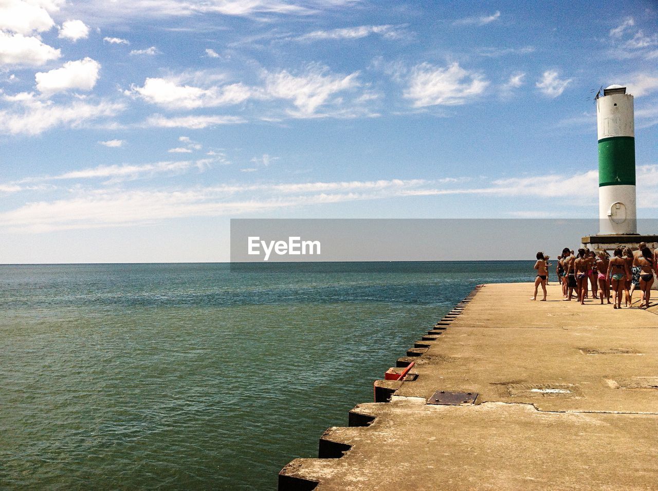 People on pier against lighthouse and lake michigan