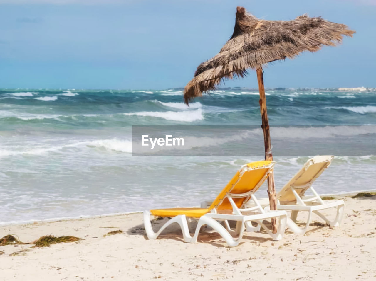 Deck chair on shore at beach against sky