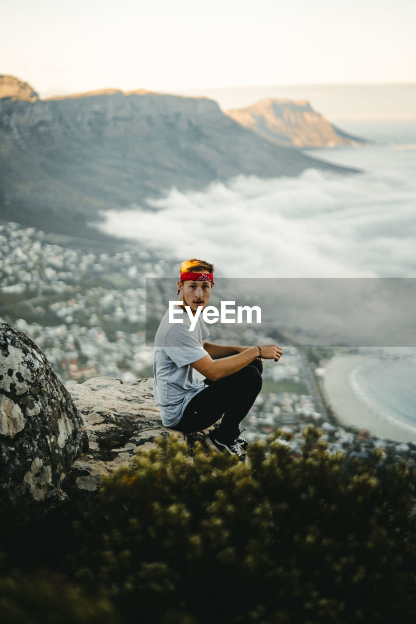 MAN SITTING ON ROCK AGAINST MOUNTAINS