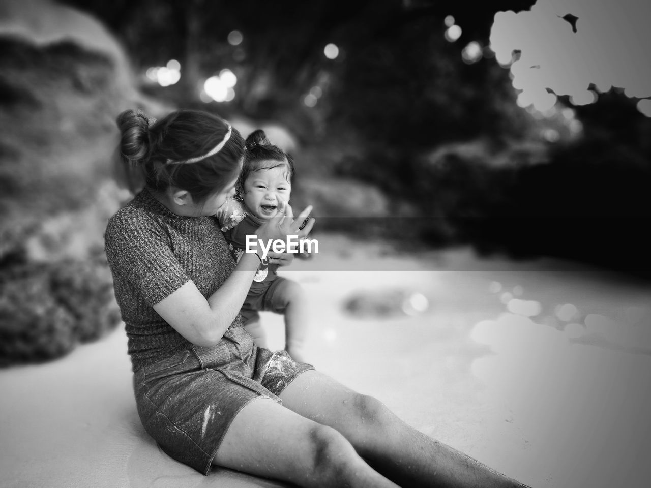 Mother playing with baby girl while sitting at beach