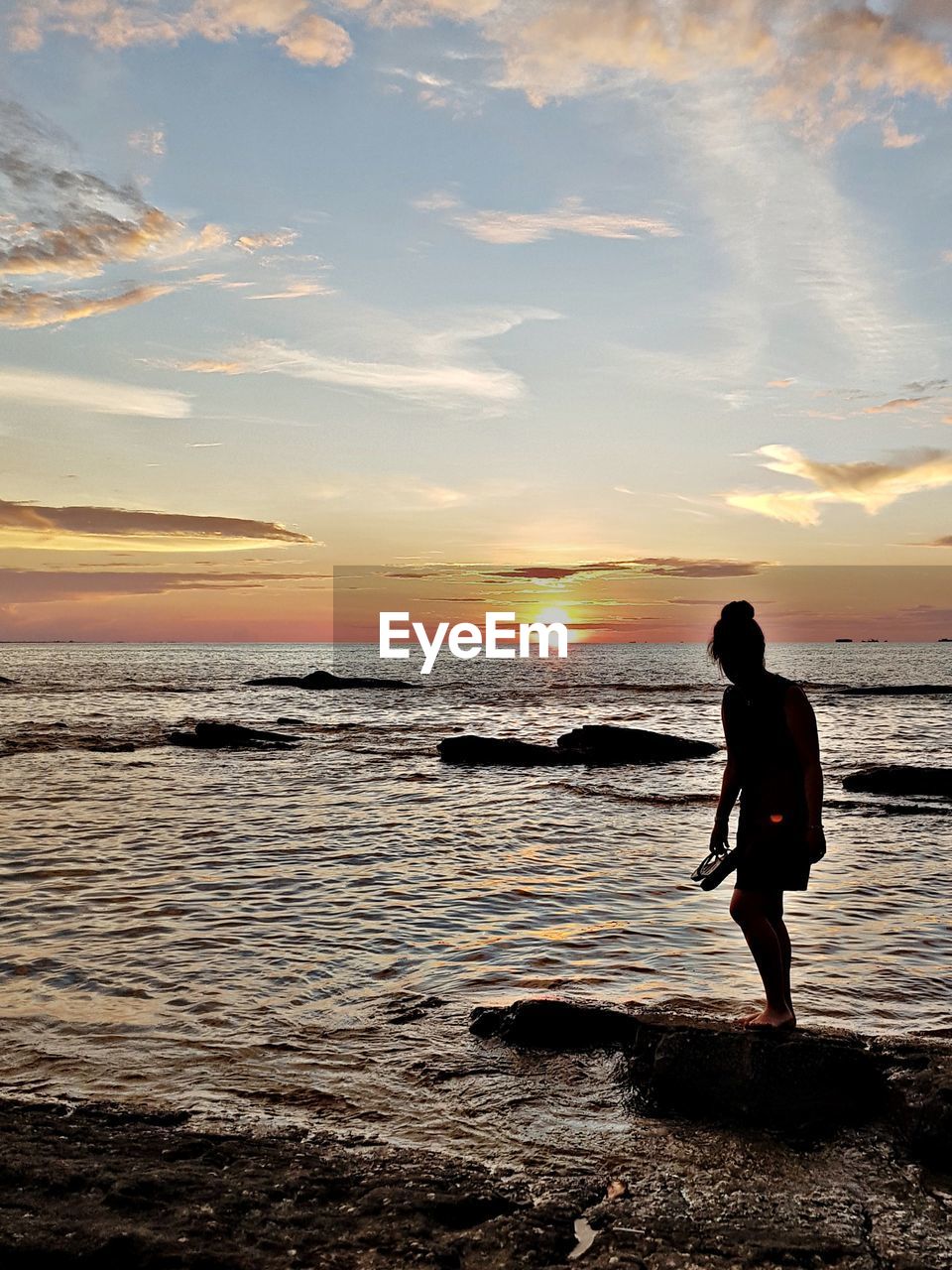 MAN STANDING AT BEACH DURING SUNSET