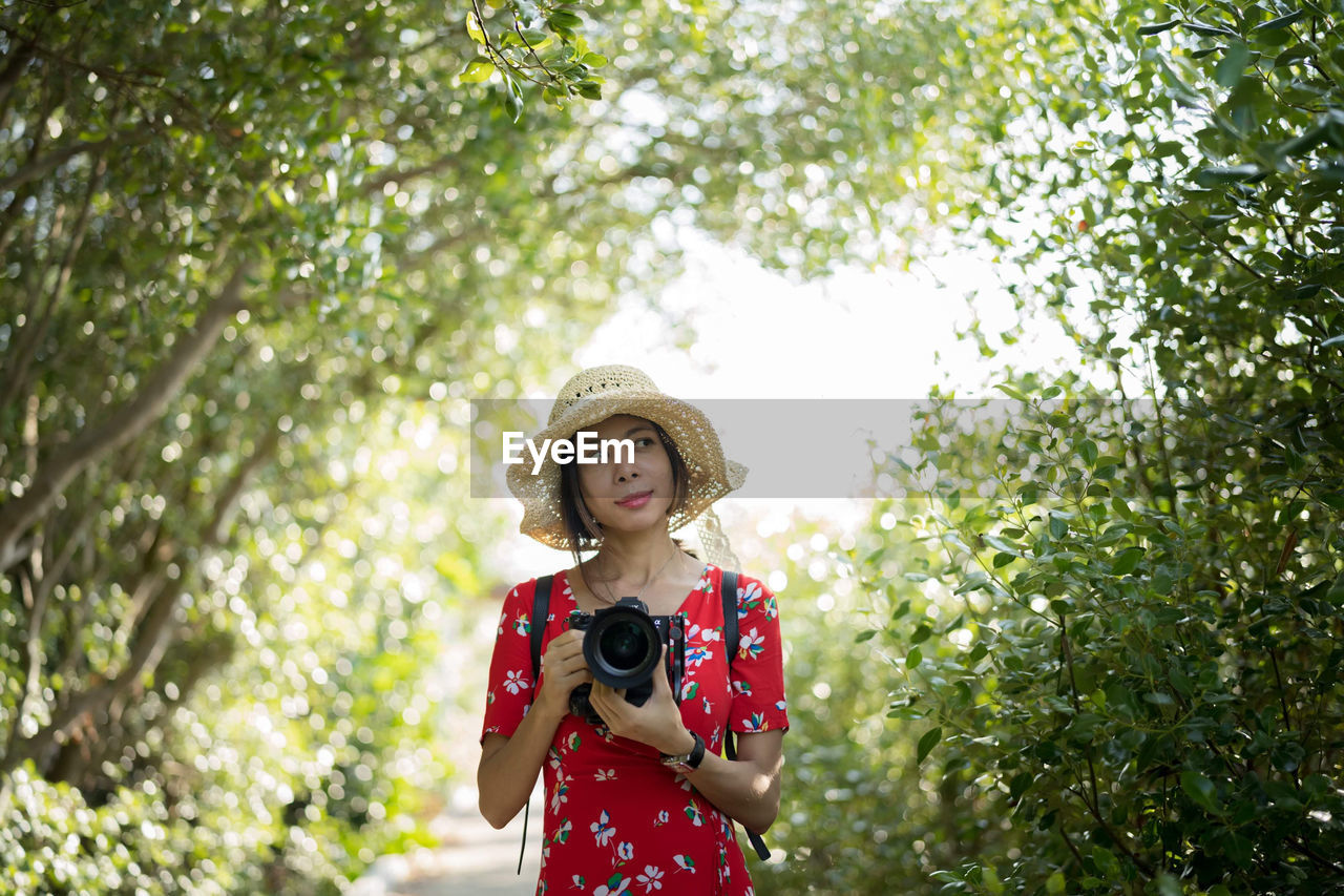 Woman holding camera standing against plants