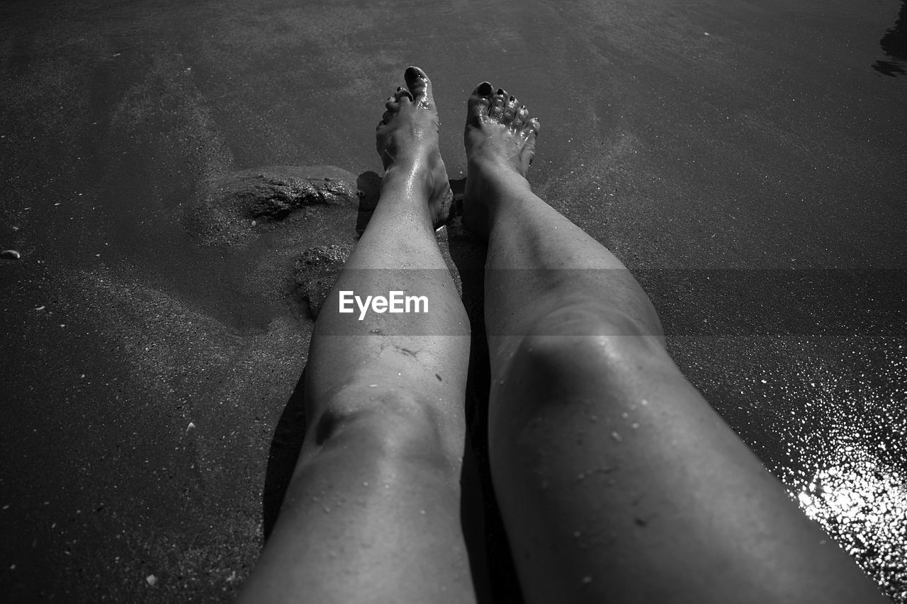 LOW SECTION OF WOMAN RELAXING ON WATER AT SHORE