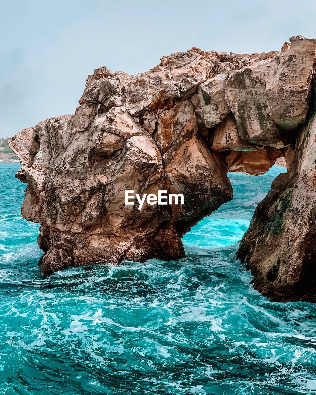 Rock formation by turquoise sea against clear blue sky