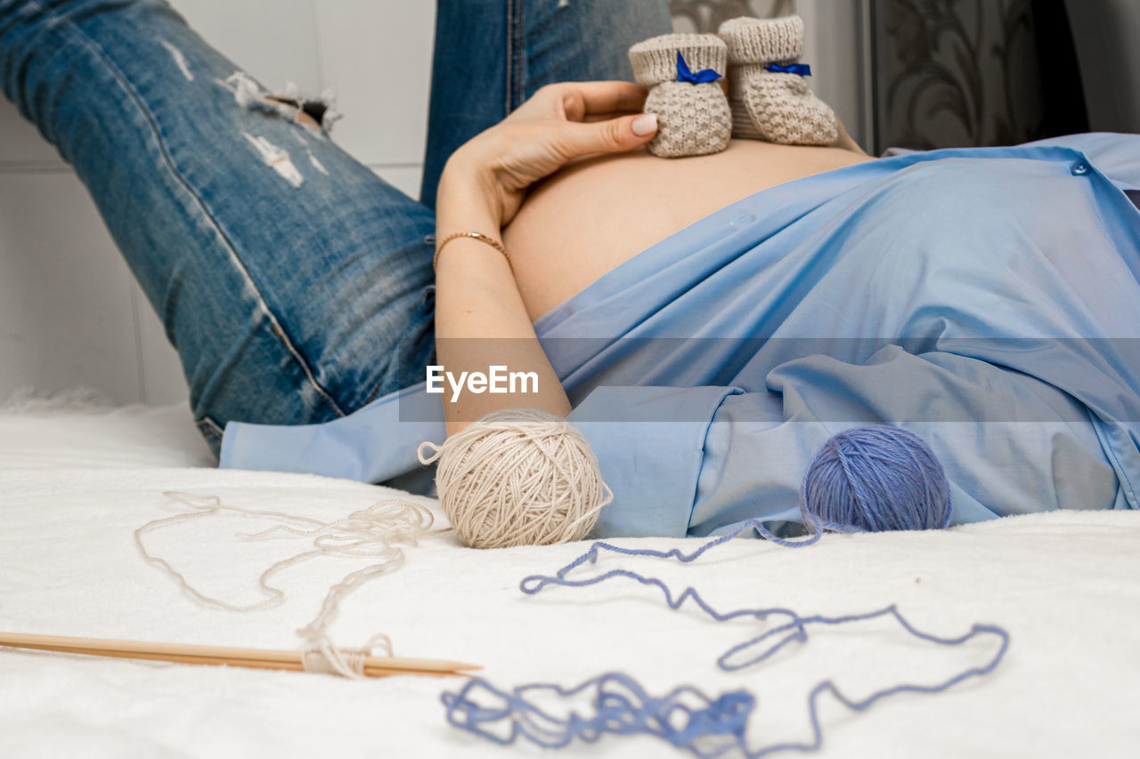 Baby booties on the belly of a pregnant woman sitting on the couch. close-up.