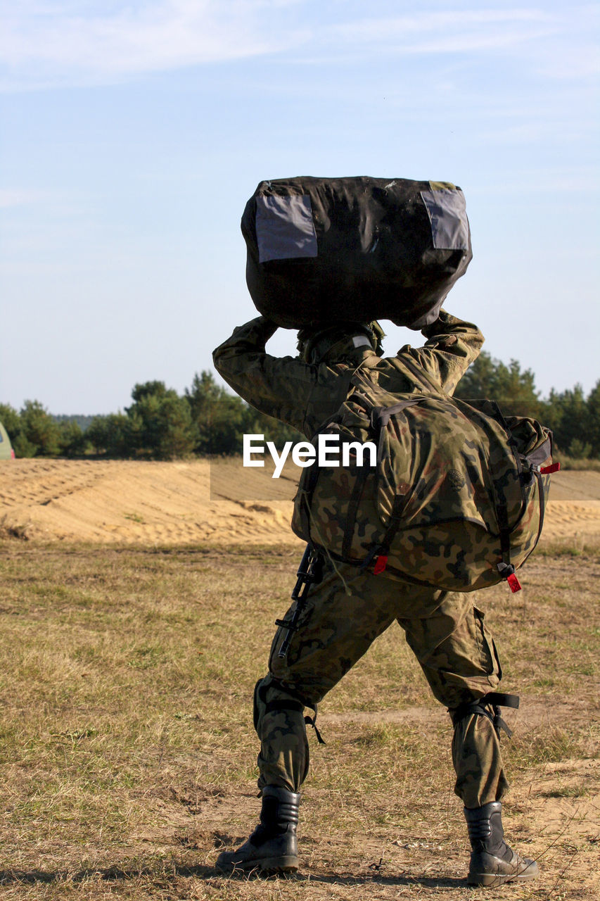 Army soldier with bags walking on field against sky