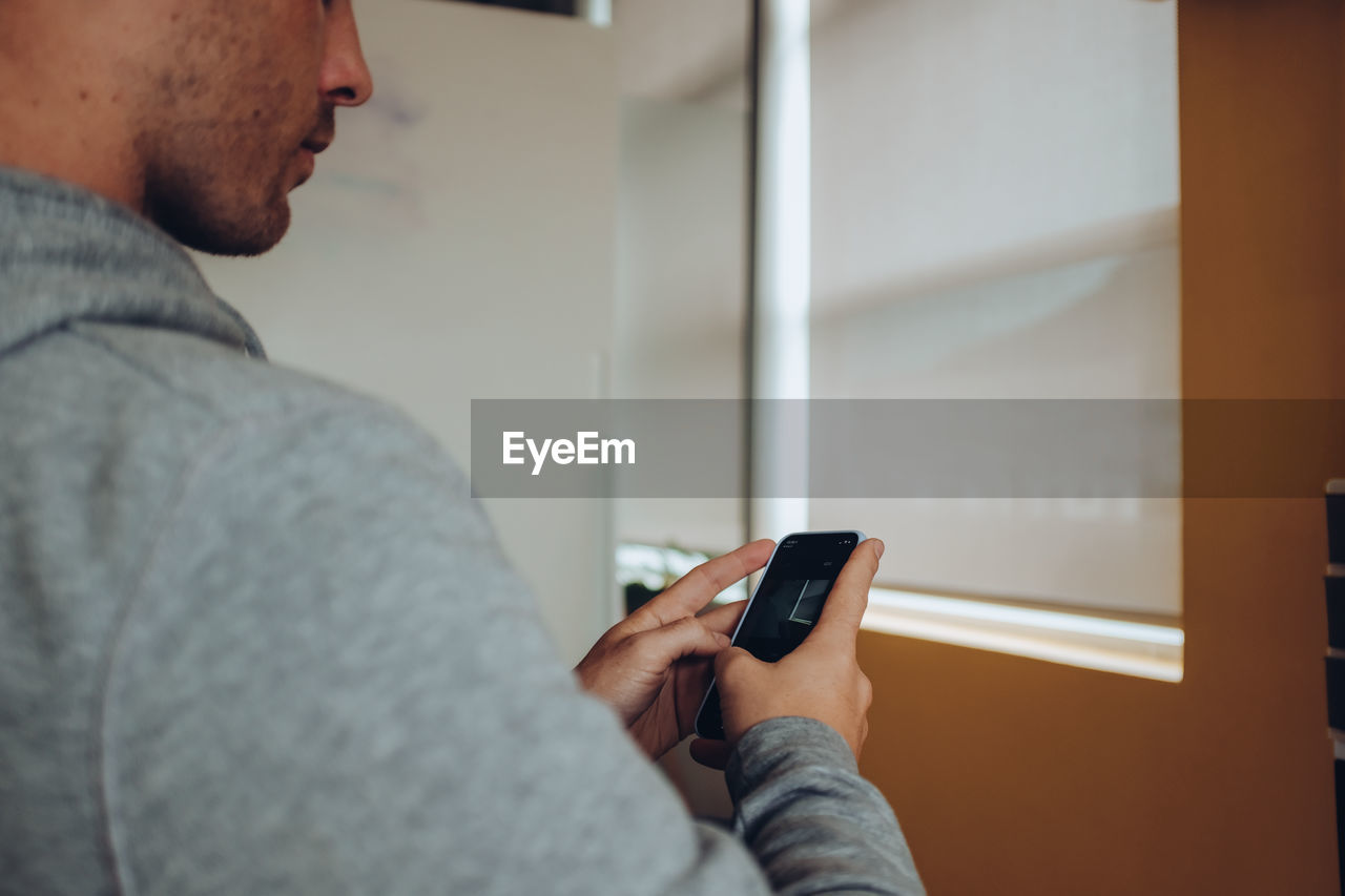 Midsection of man using mobile phone while sitting indoors