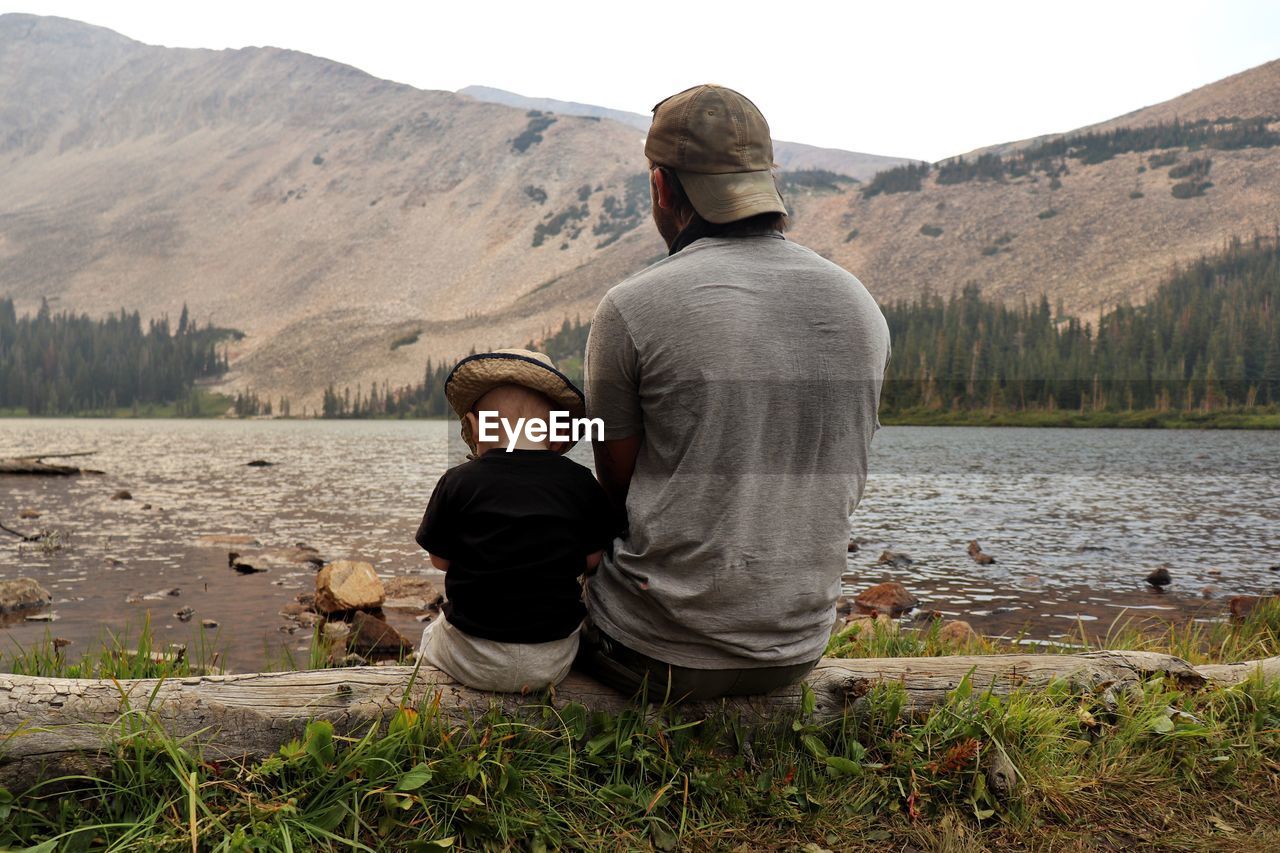 A father and son sit together, enjoying the view they had earned from a hike through the mountains. 
