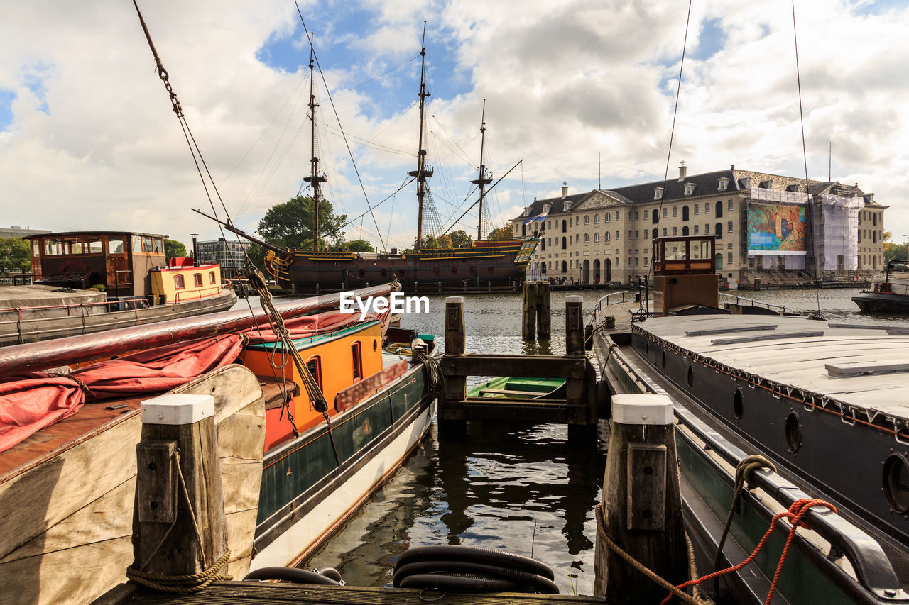 Sailboats moored on canal amidst buildings in city against sky