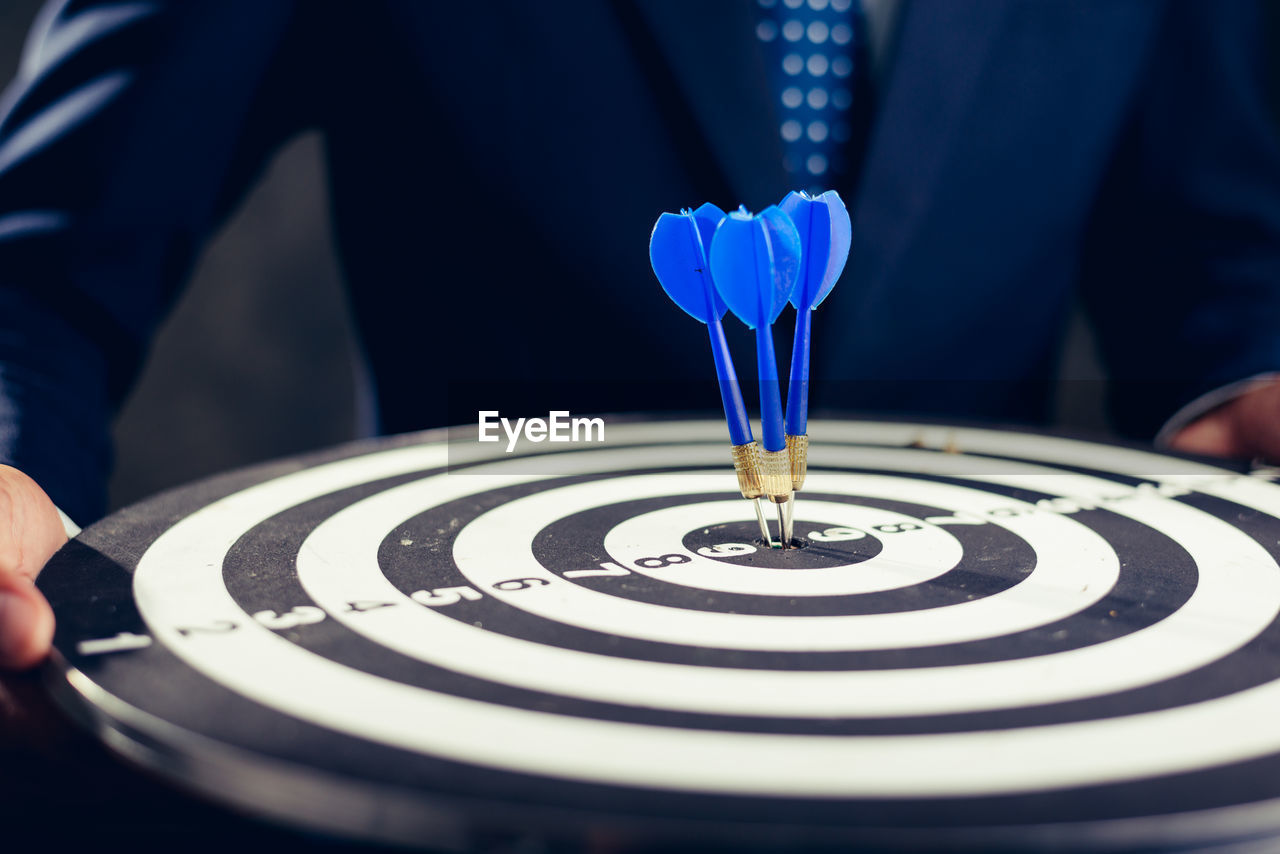 Midsection of businessman holding dartboard wit arrows