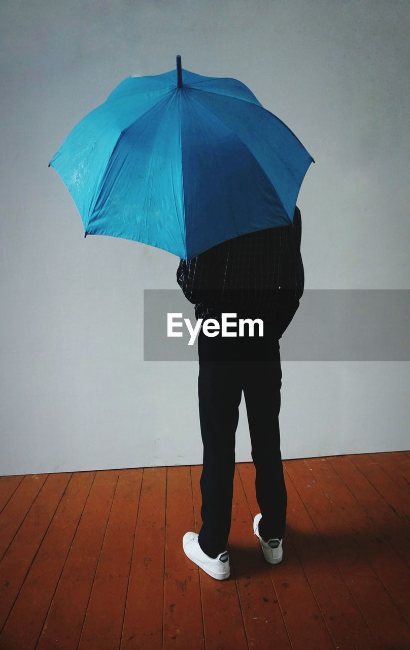 Low section of man holding umbrella standing against wall