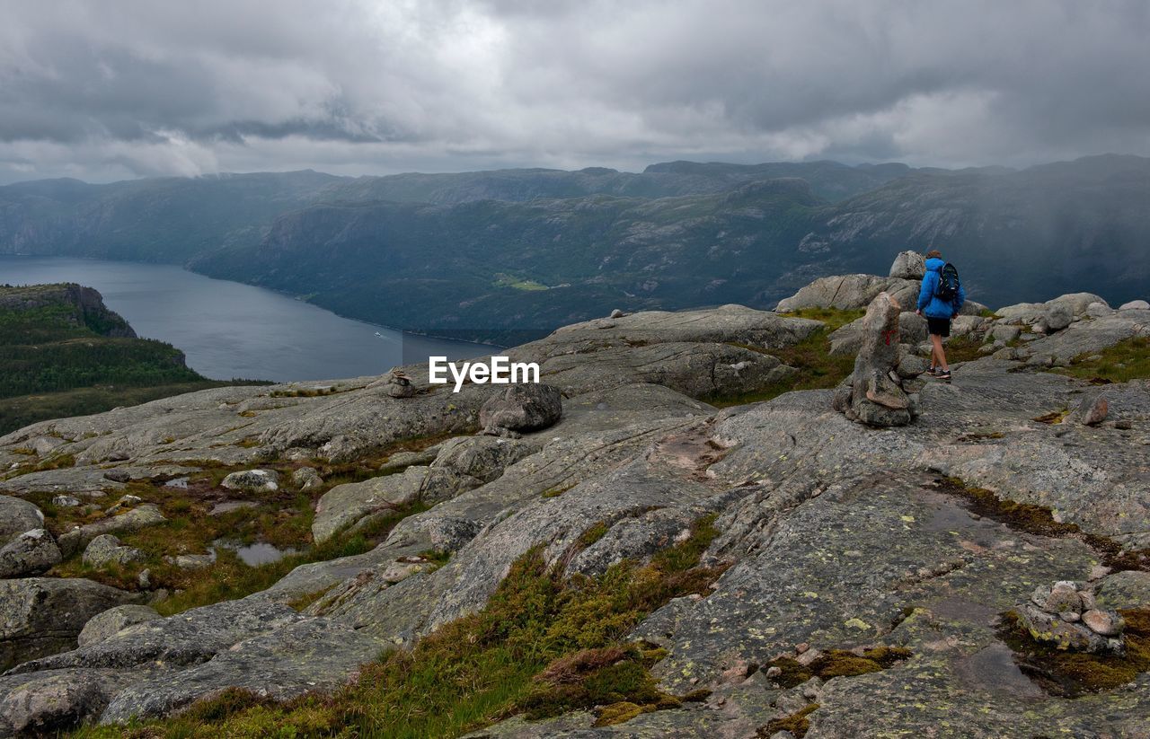 Man hiking on rock by mountains and fjord against sky